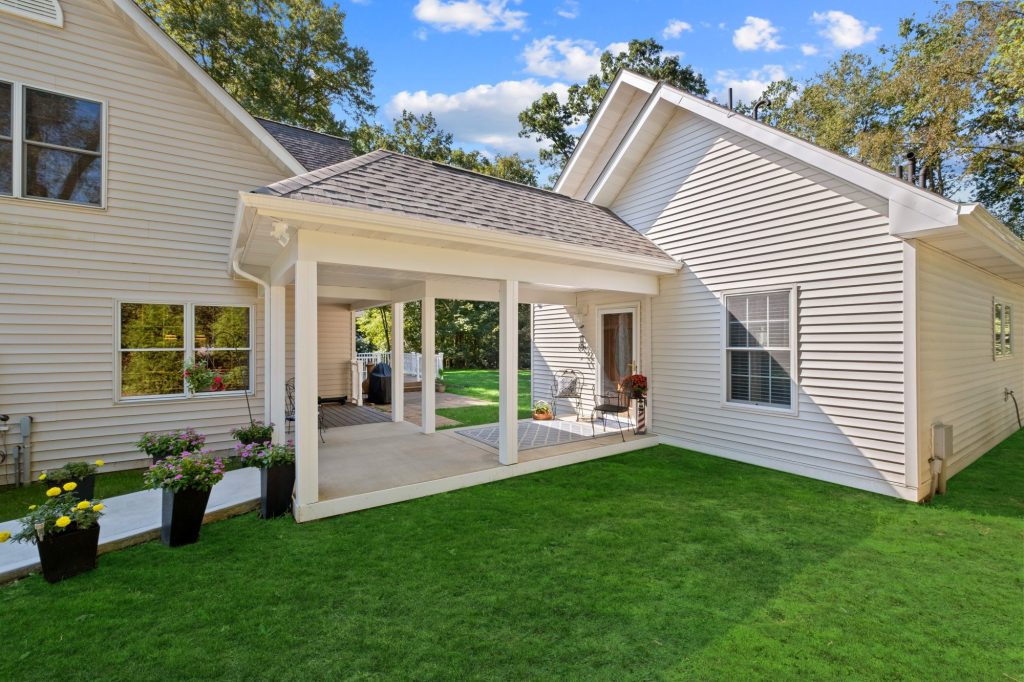 Single-story beige house with a covered walkway, white trim, potted plants, and green lawn under a blue sky—an inviting multi-generational home design perfect for family living.