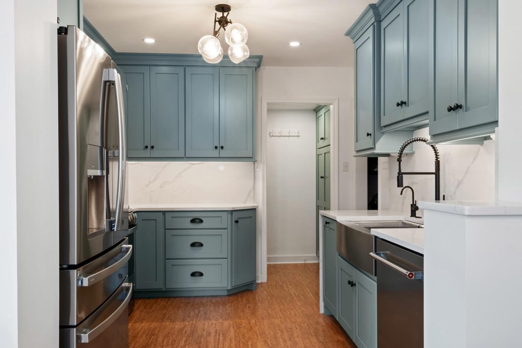 Modern kitchen with blue cabinetry, stainless steel appliances, farmhouse sink, marble backsplash, and wood flooring under bright ceiling lights—perfect inspiration for home additions Pittsburgh homeowners will love.