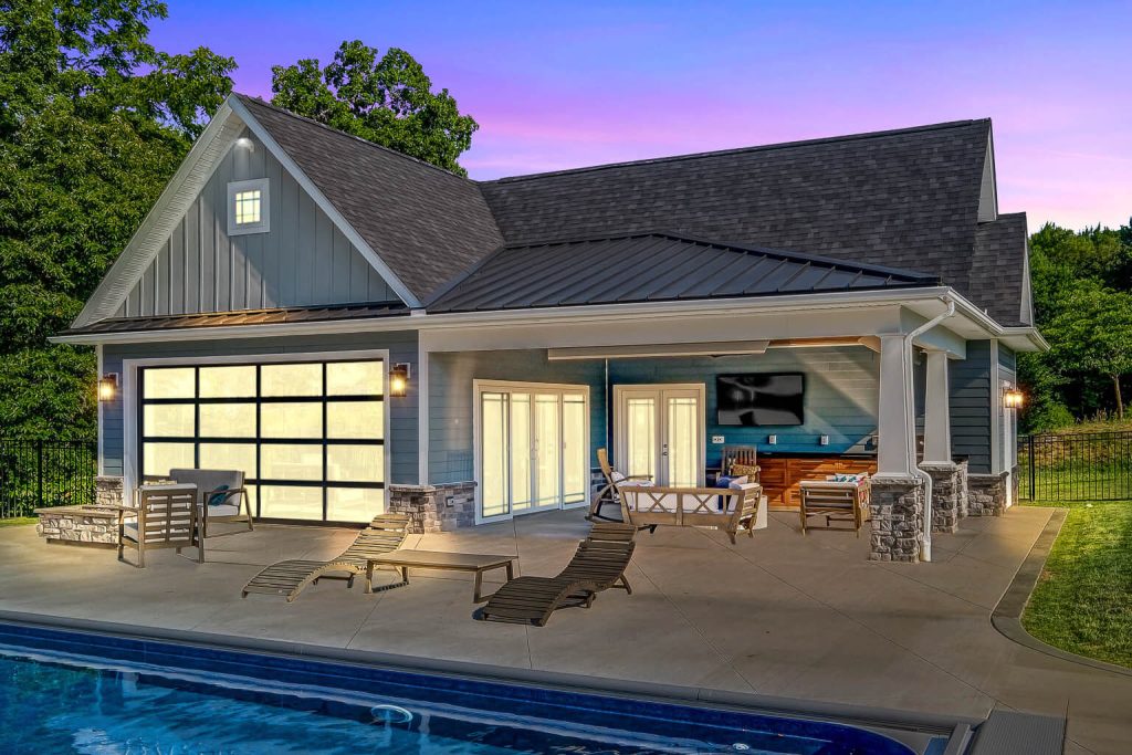 Modern pool house with patio furniture, large windows, and an outdoor seating area beside a swimming pool at dusk—perfect inspiration for home additions Pittsburgh homeowners will love.