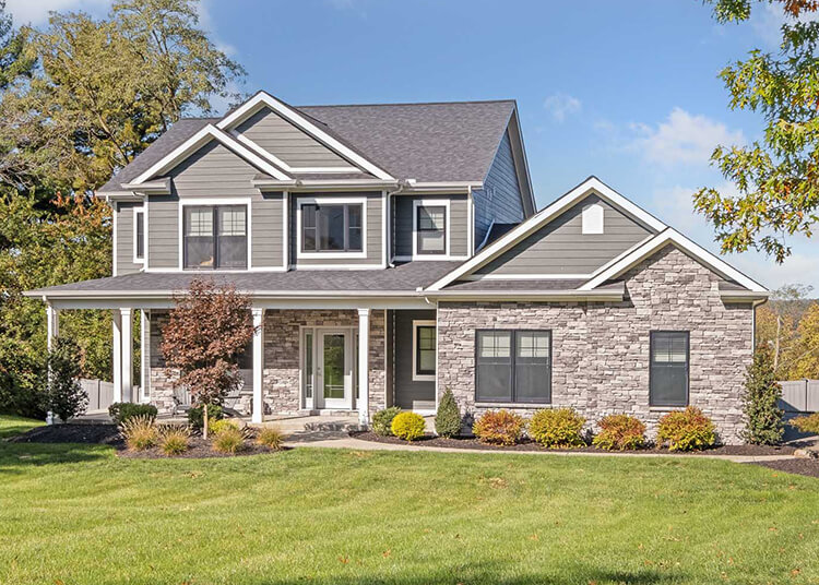 Two-story suburban house with gray siding, stone accents, white trim, large front windows, and landscaped yard—expertly crafted by a custom home builder Pittsburgh families trust.