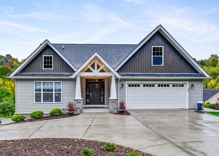 A modern single-story house with gray siding, white trim, a covered front porch, and a double garage, set on a concrete driveway with minimal landscaping.